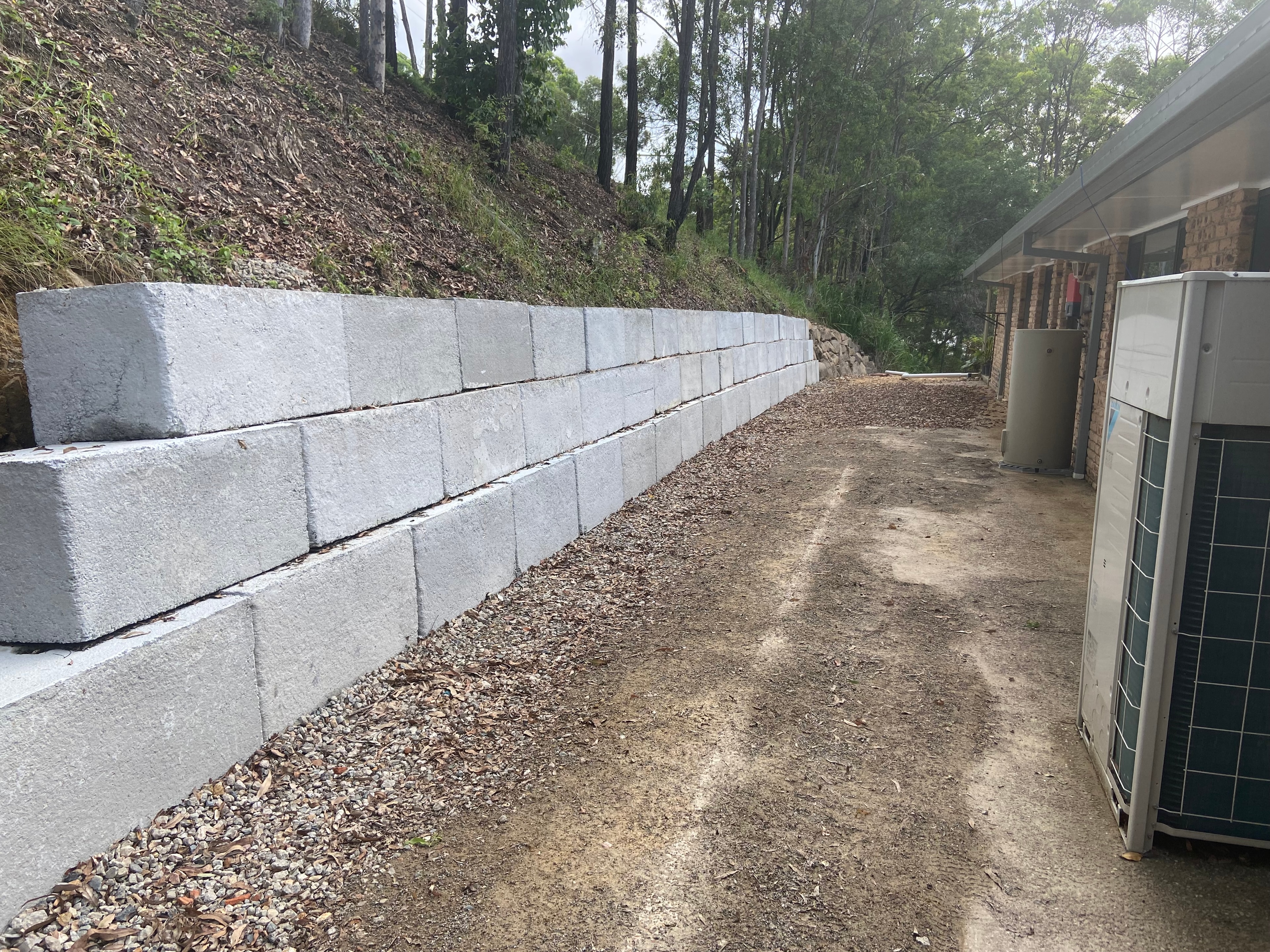 Long concrete block retaining wall beside house with bushland backdrop