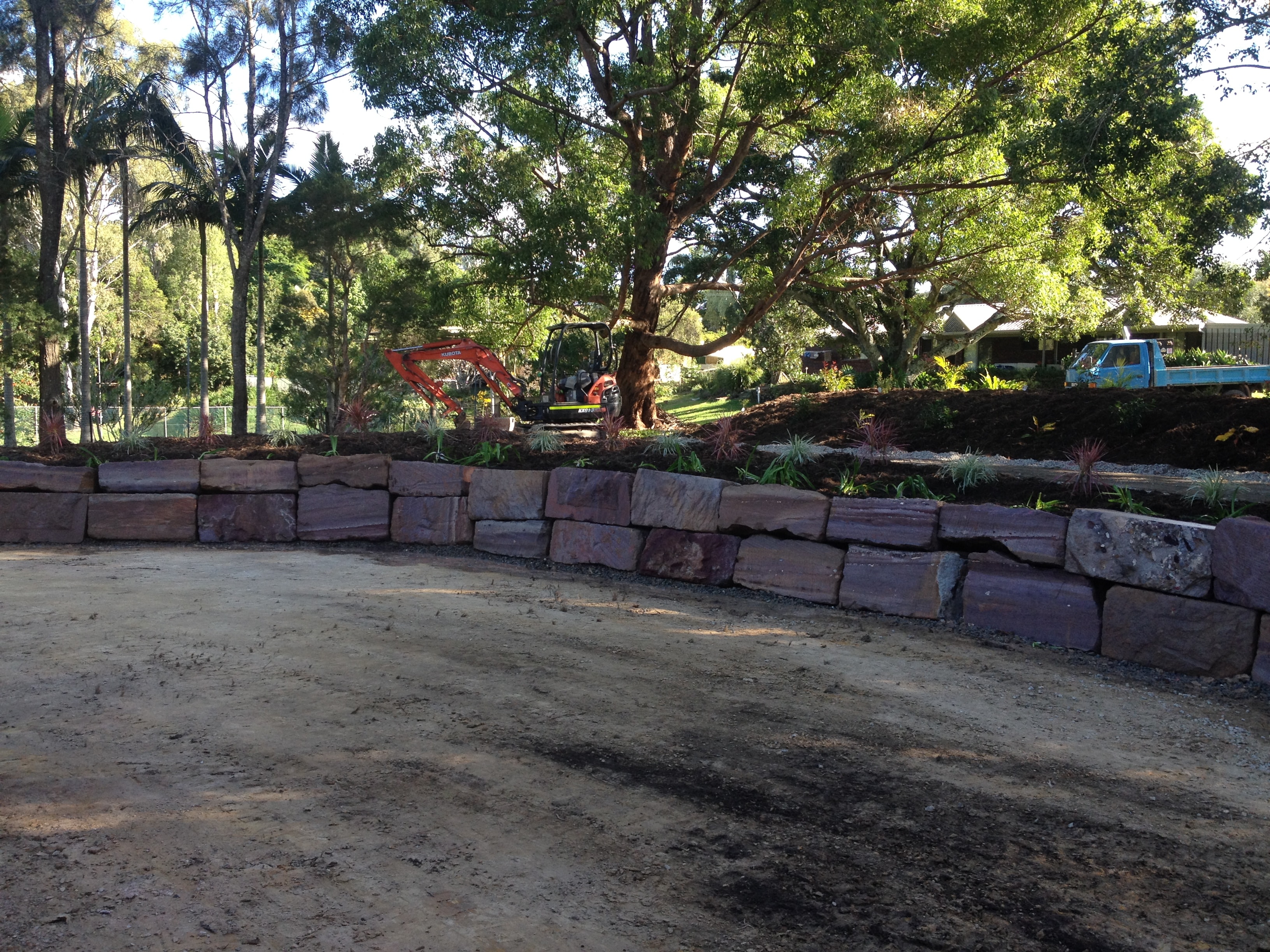 Curved sandstone block retaining wall with Kubota excavator and truck