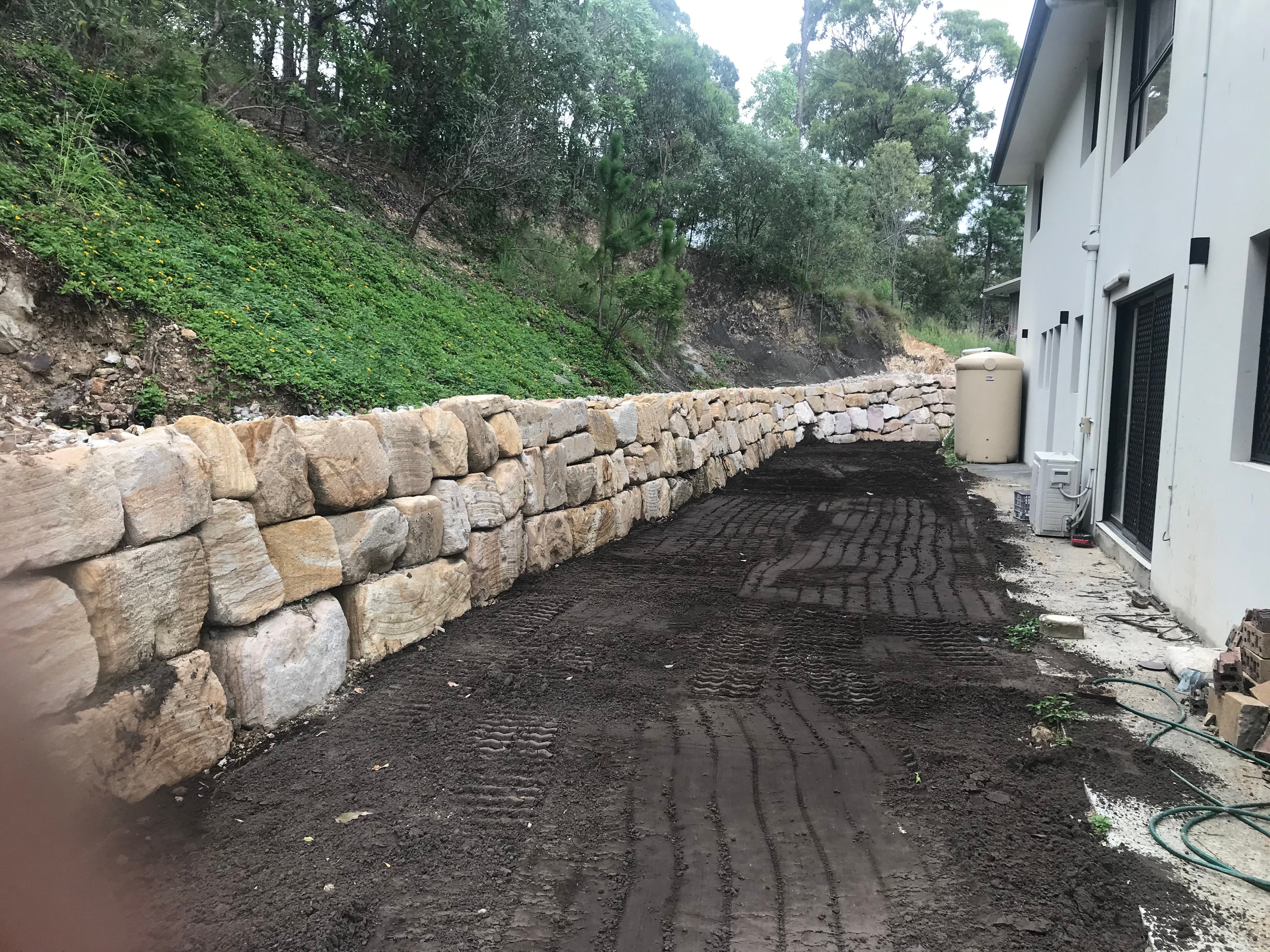 Long sandstone boulder retaining wall beside white rendered house