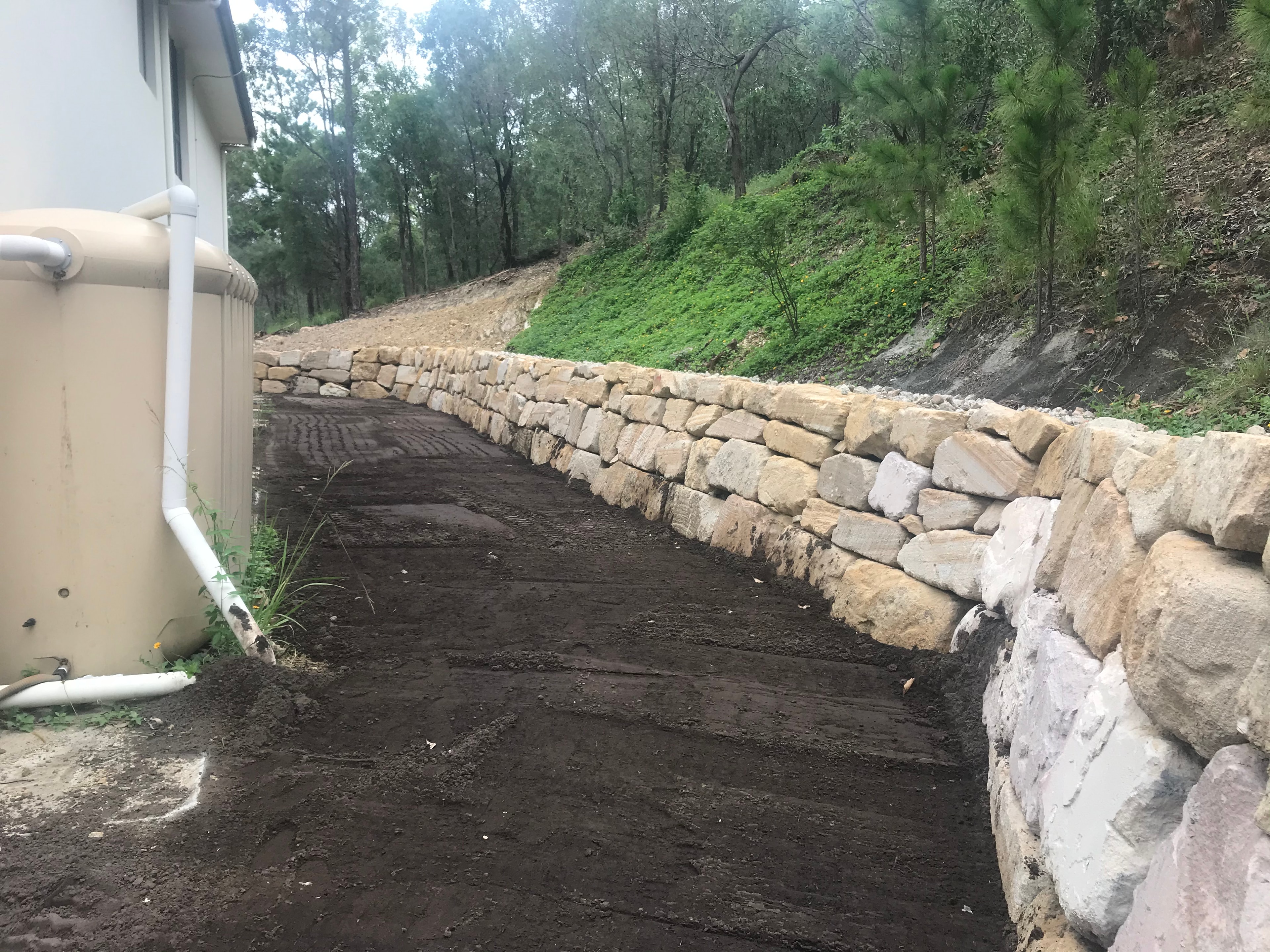 Sandstone rock retaining wall with freshly graded soil beside house
