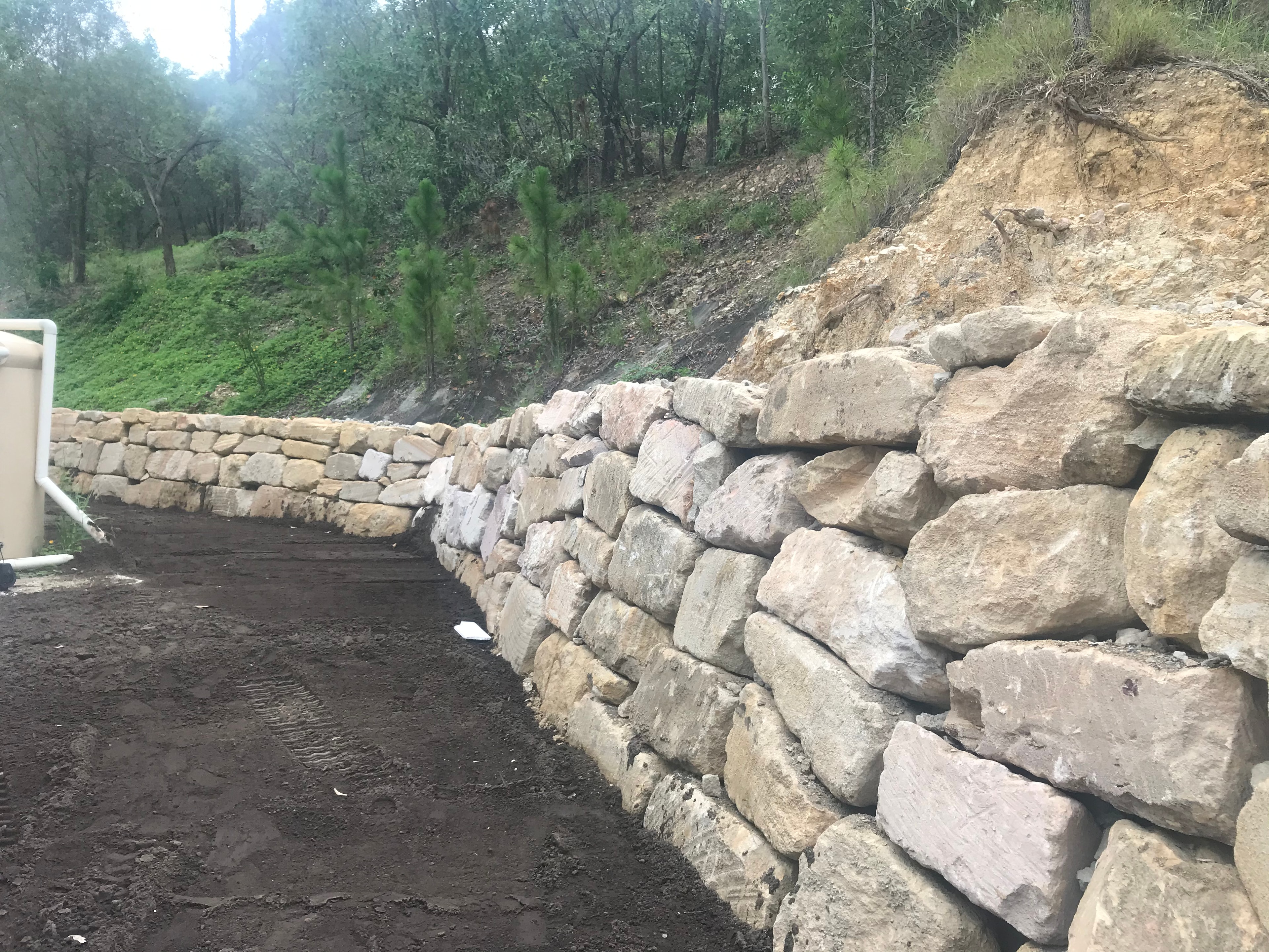 Natural stone retaining wall with gravel drainage and bushland backdrop