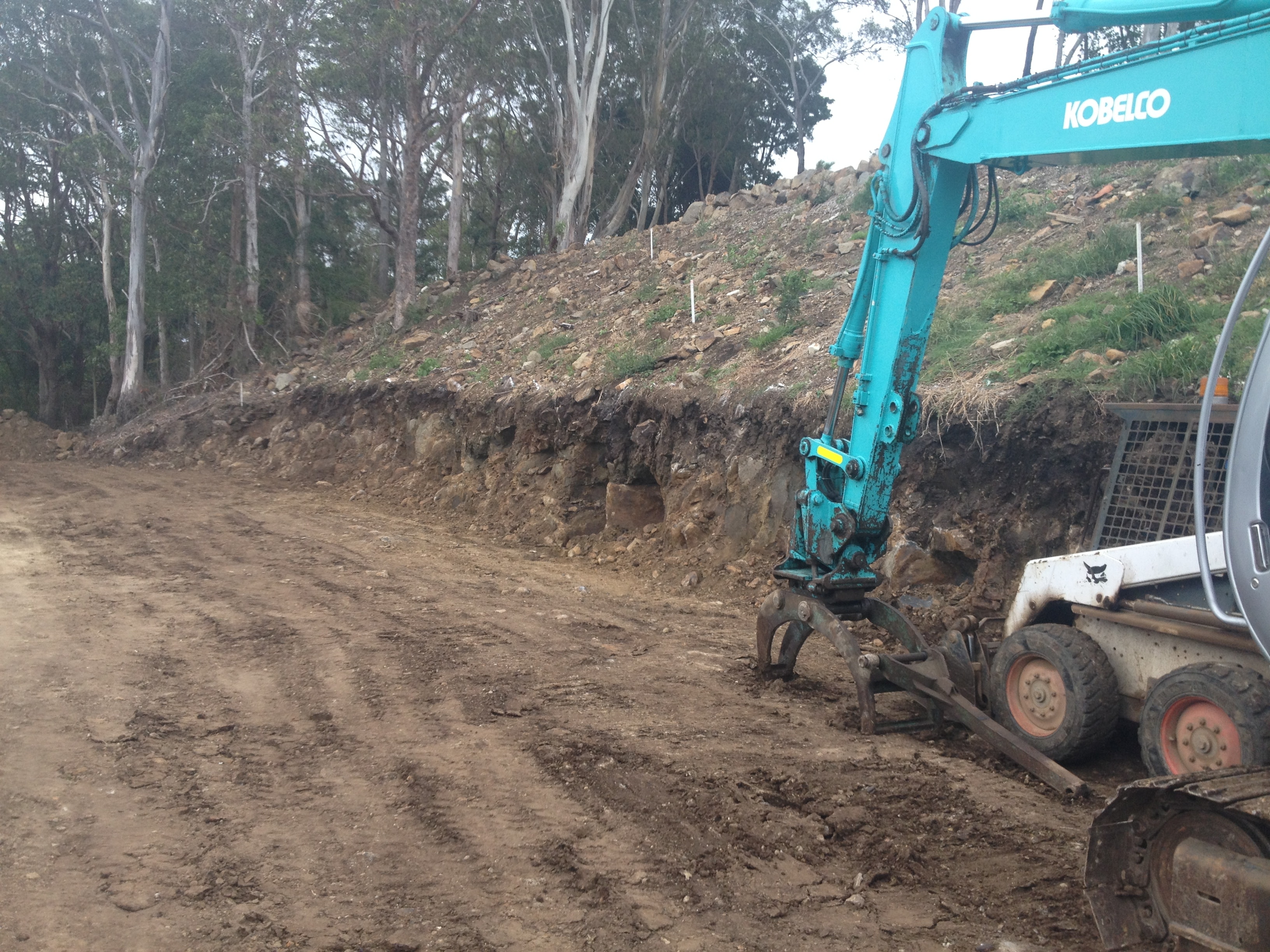 Kobelco excavator on hillside clearing site for rock wall construction