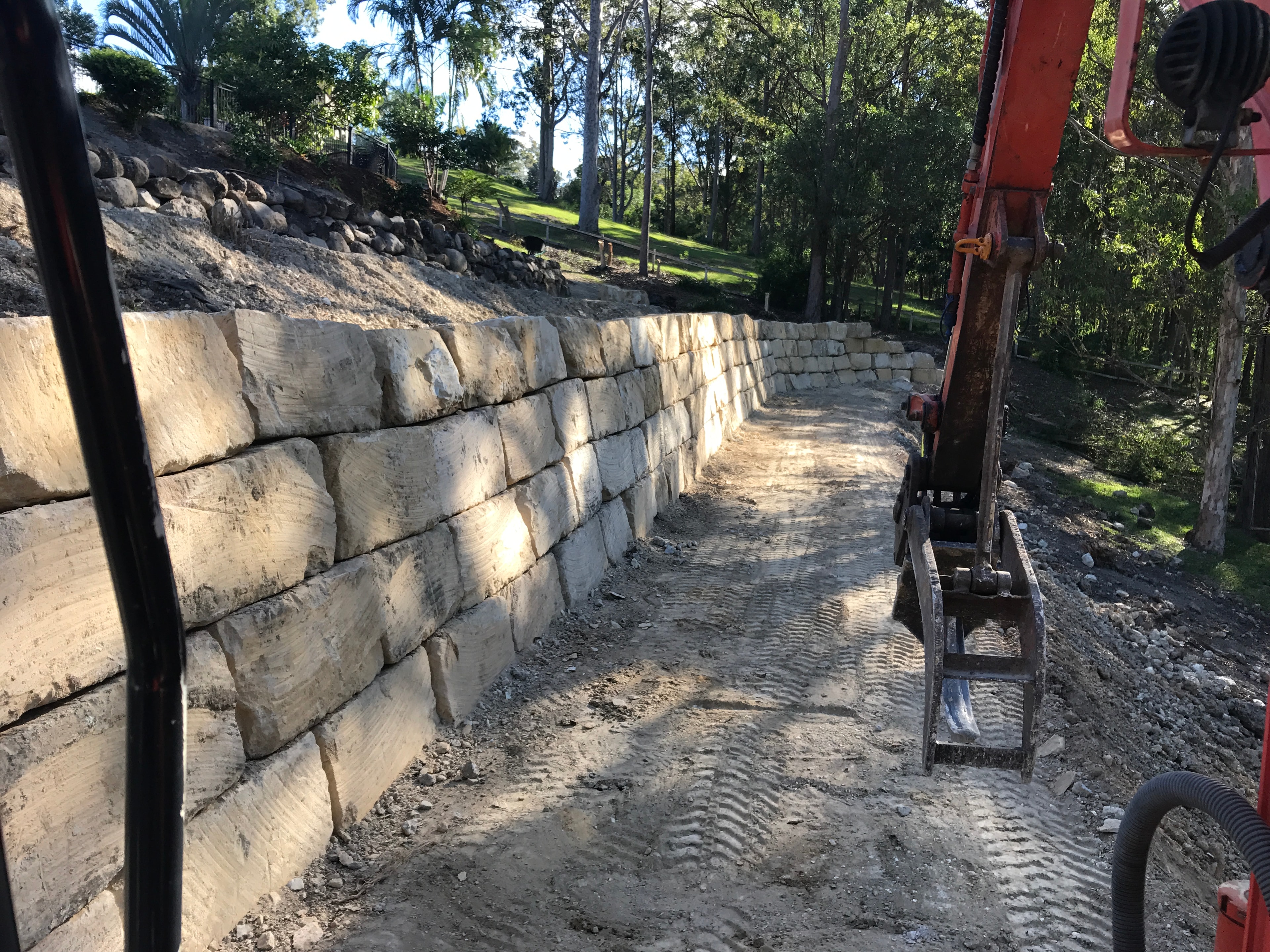 Completed sandstone retaining wall with excavator alongside driveway