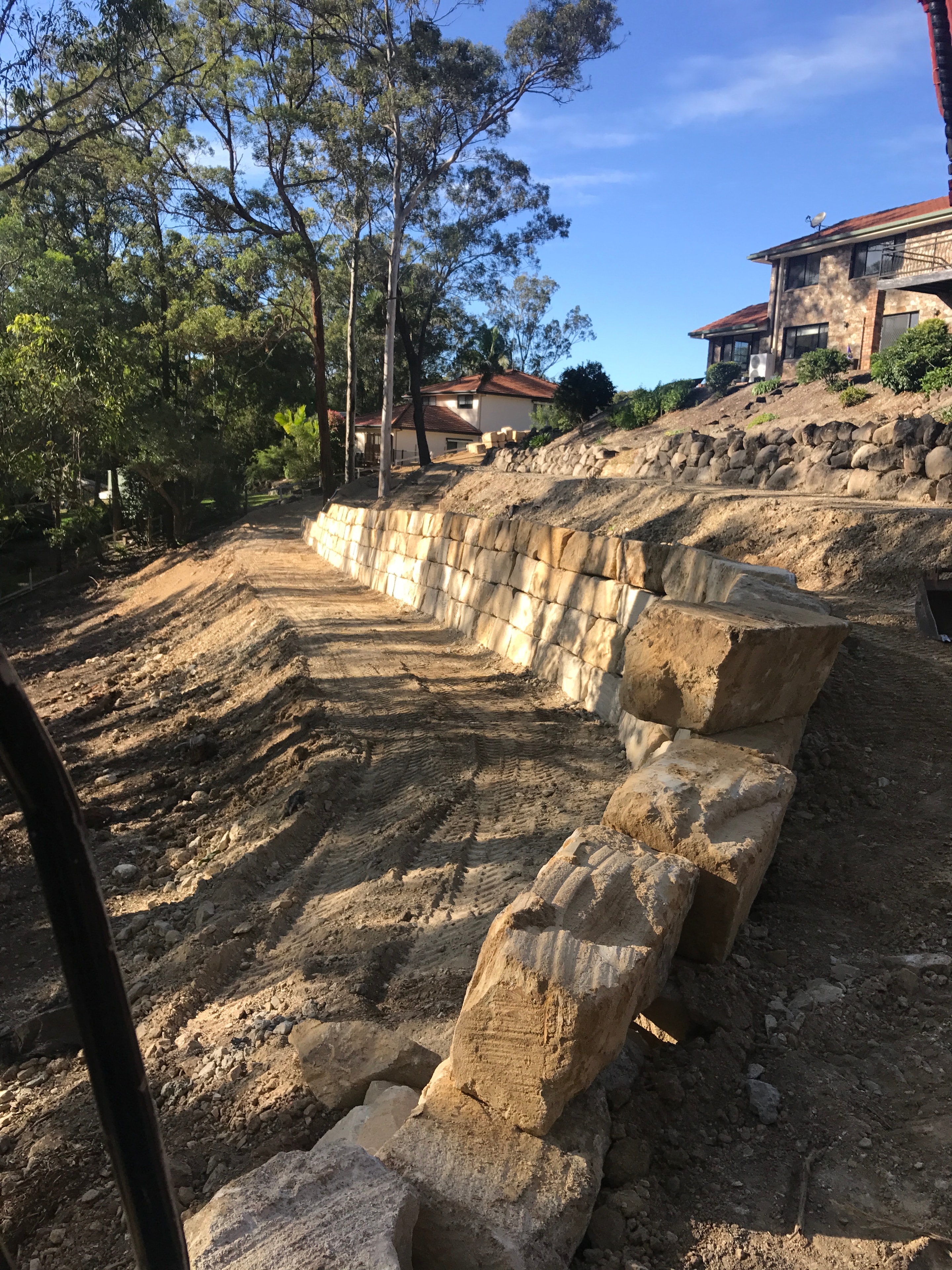 Sandstone block wall under construction beside house with boulder wall above