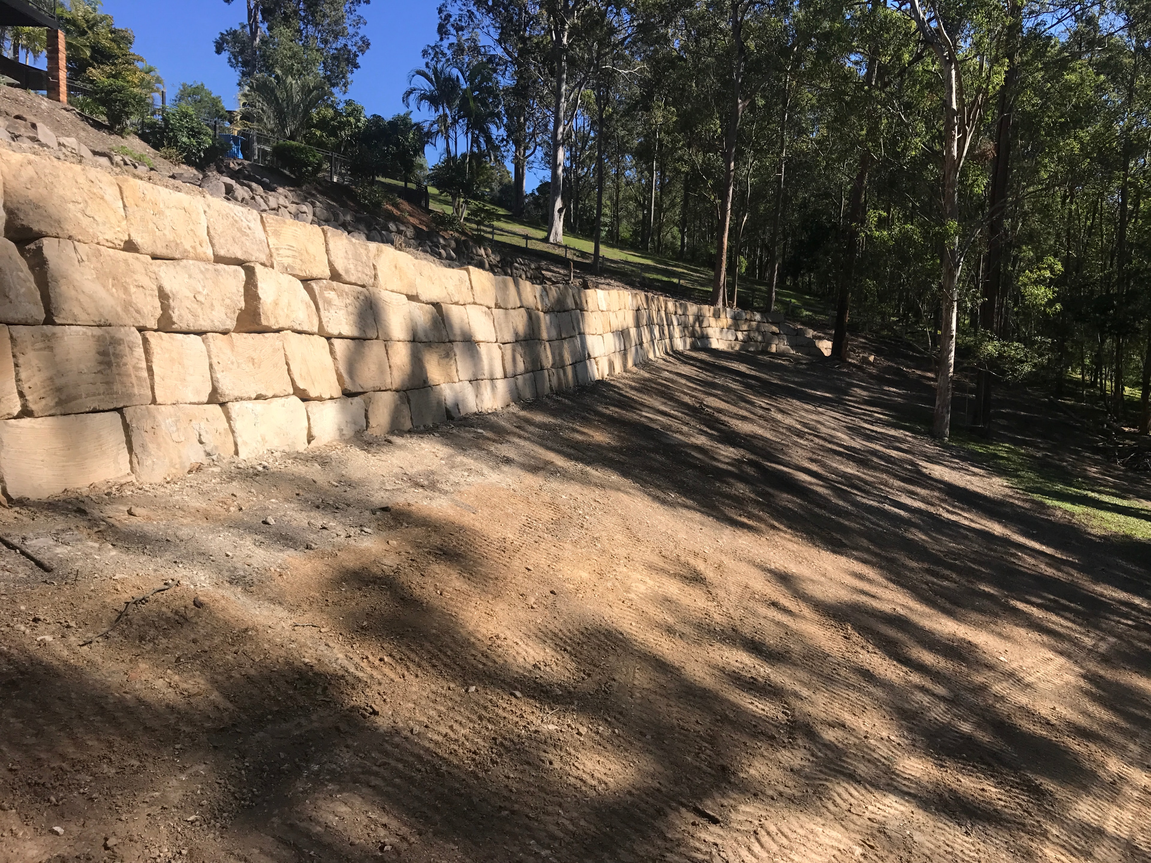 Long sandstone block retaining wall with graded pad and bushland backdrop