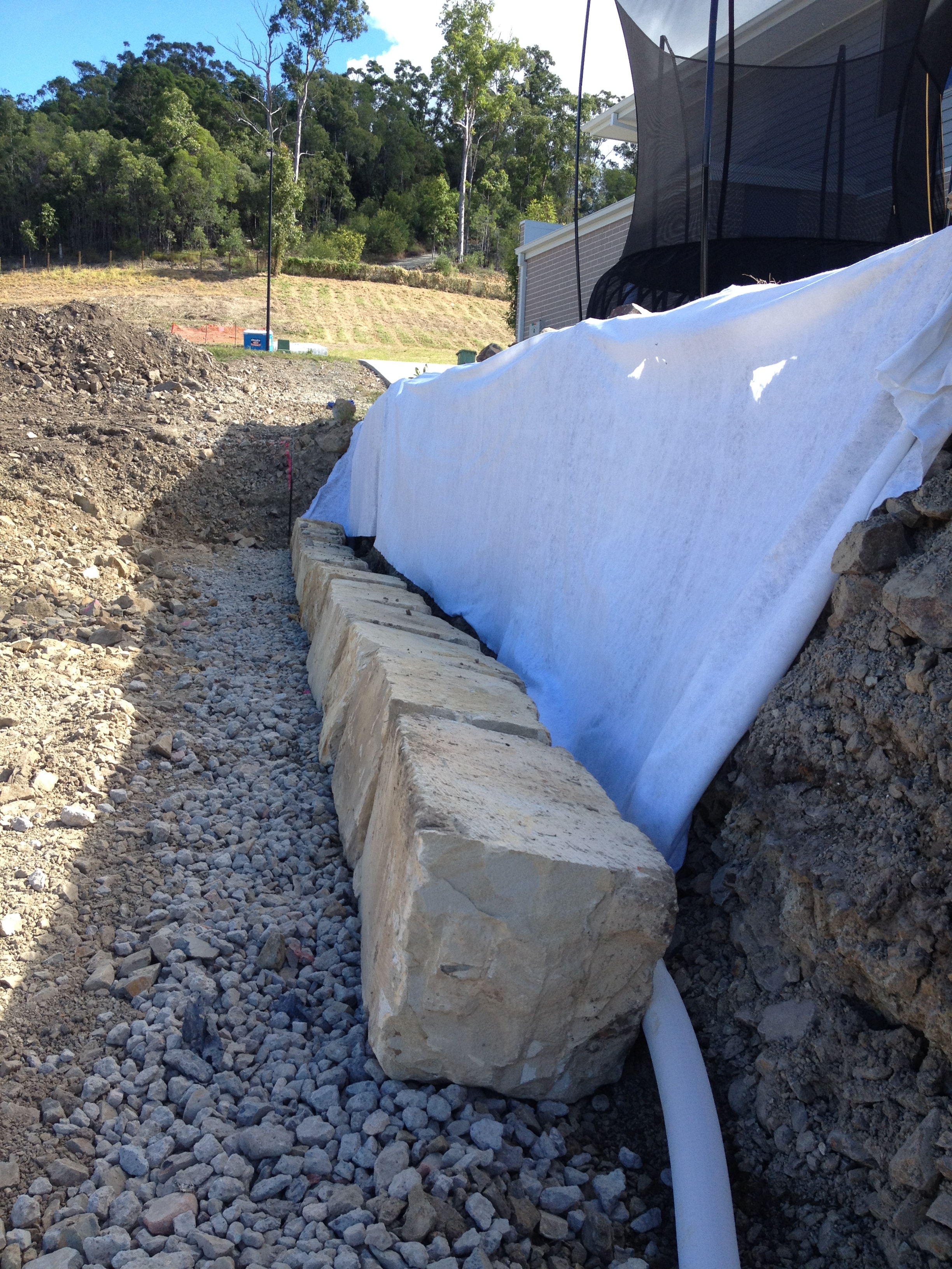 Sandstone block wall with geotextile fabric and gravel drainage under tarp