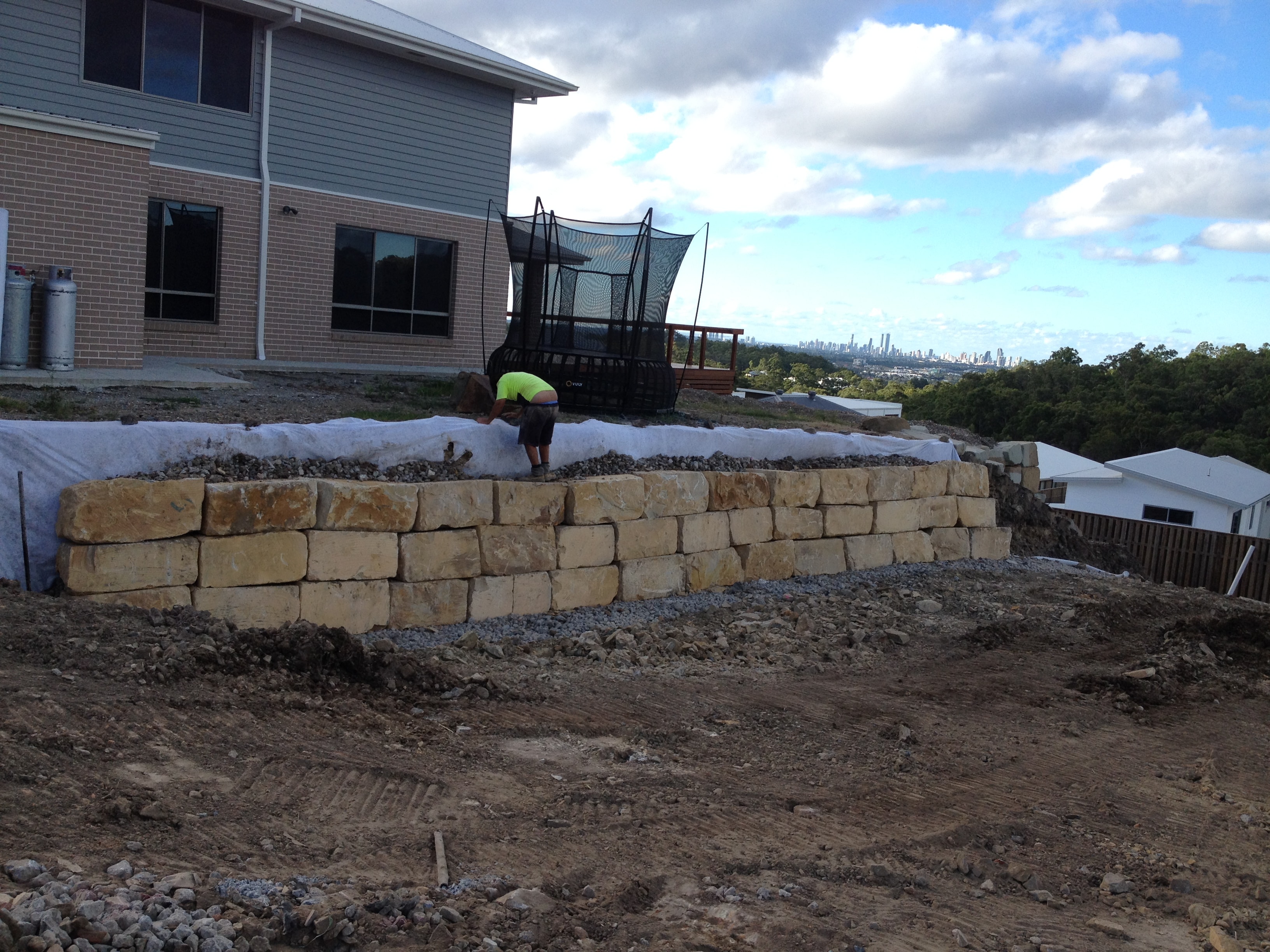 Sandstone block retaining wall being built with Gold Coast skyline