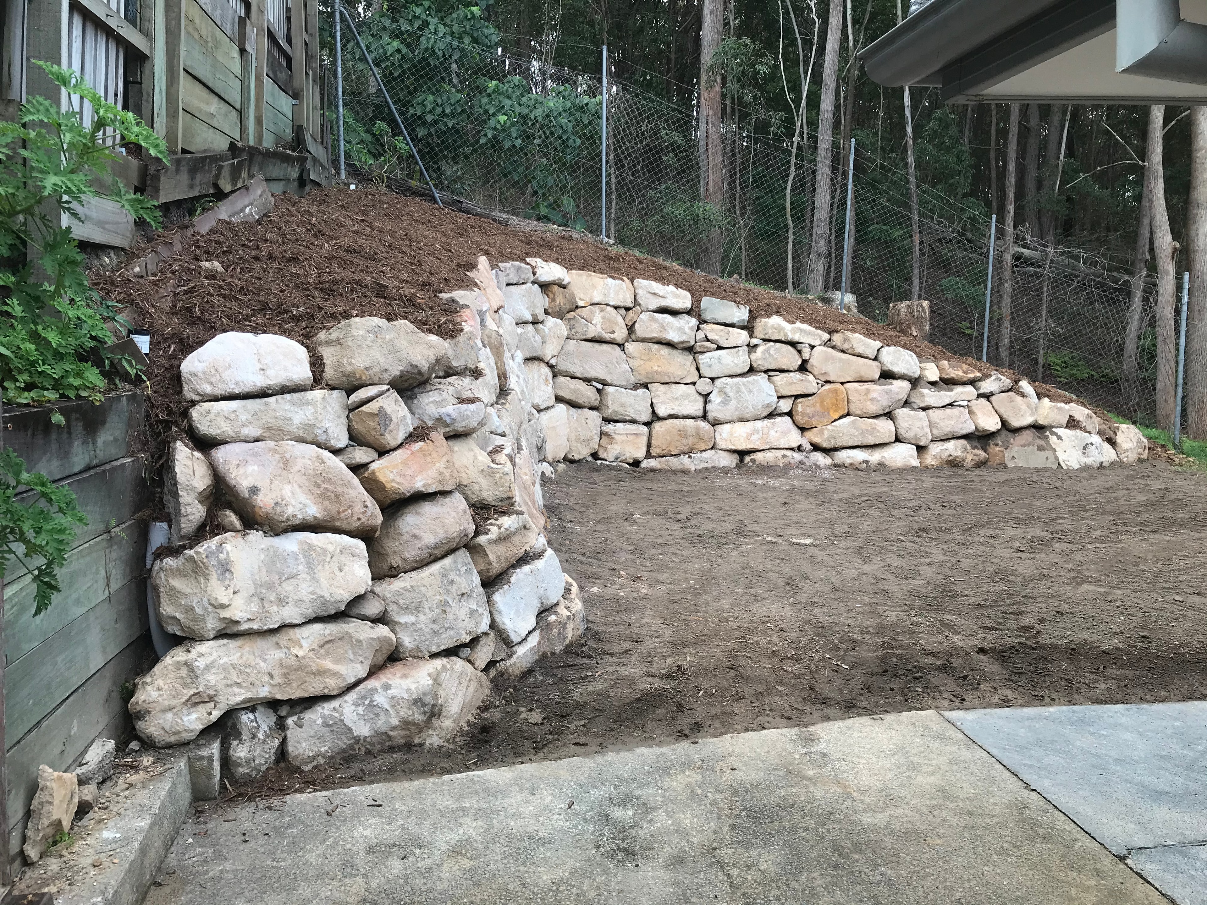Completed sandstone rock retaining wall with mulch backfill