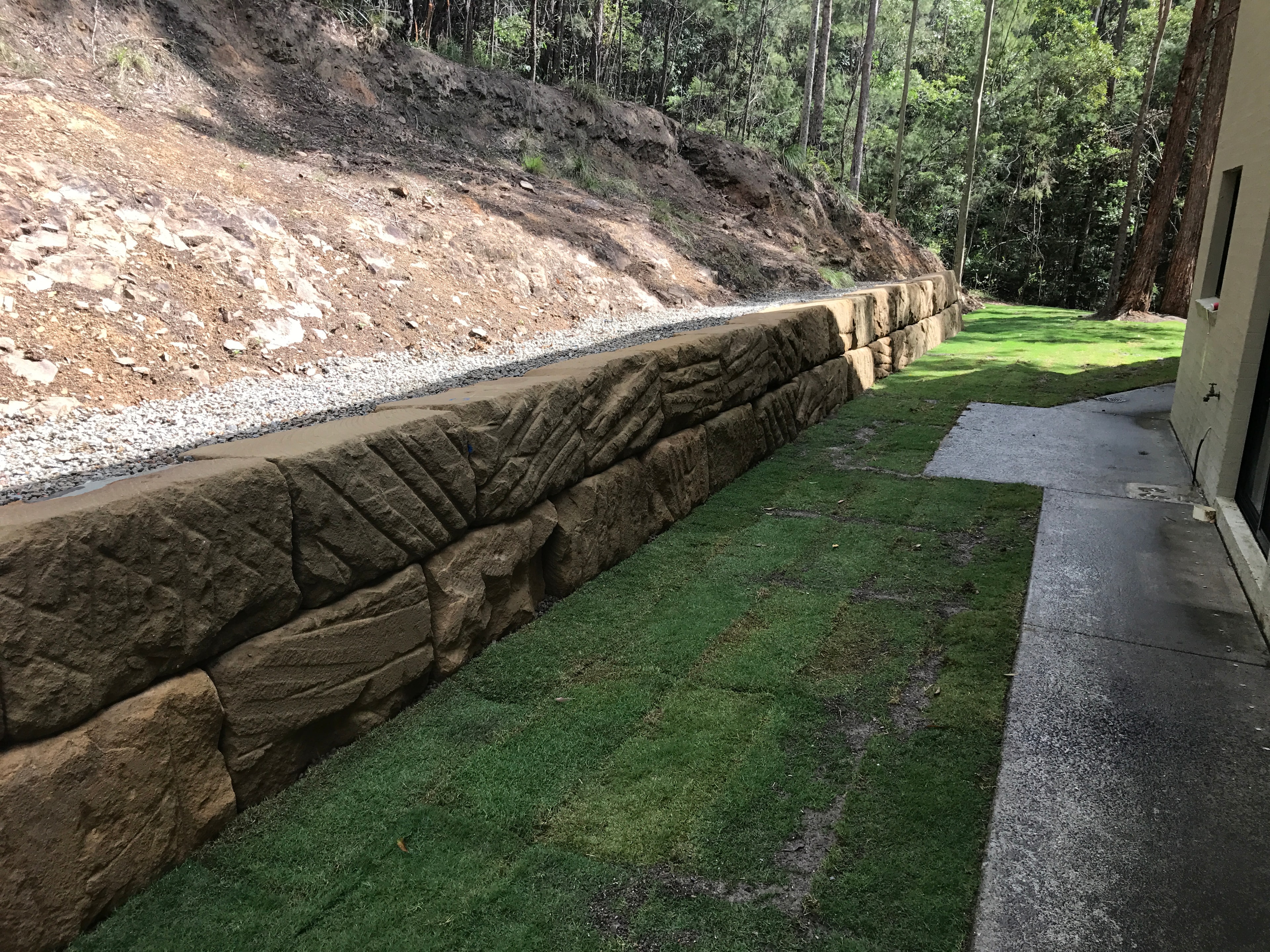 Long sandstone retaining wall with lawn and bushland backdrop