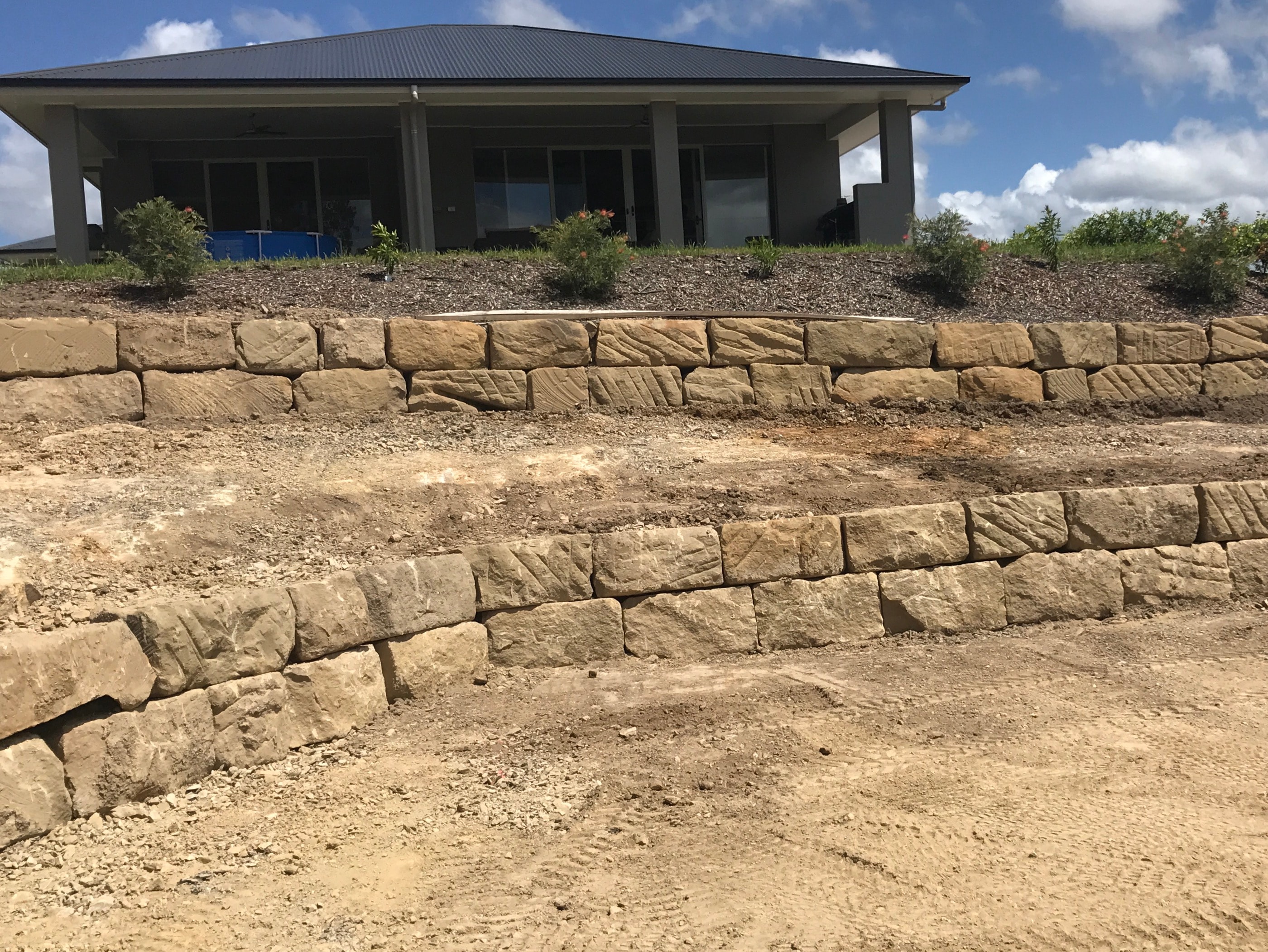 Two-tier sandstone block retaining walls with graded yard and house behind