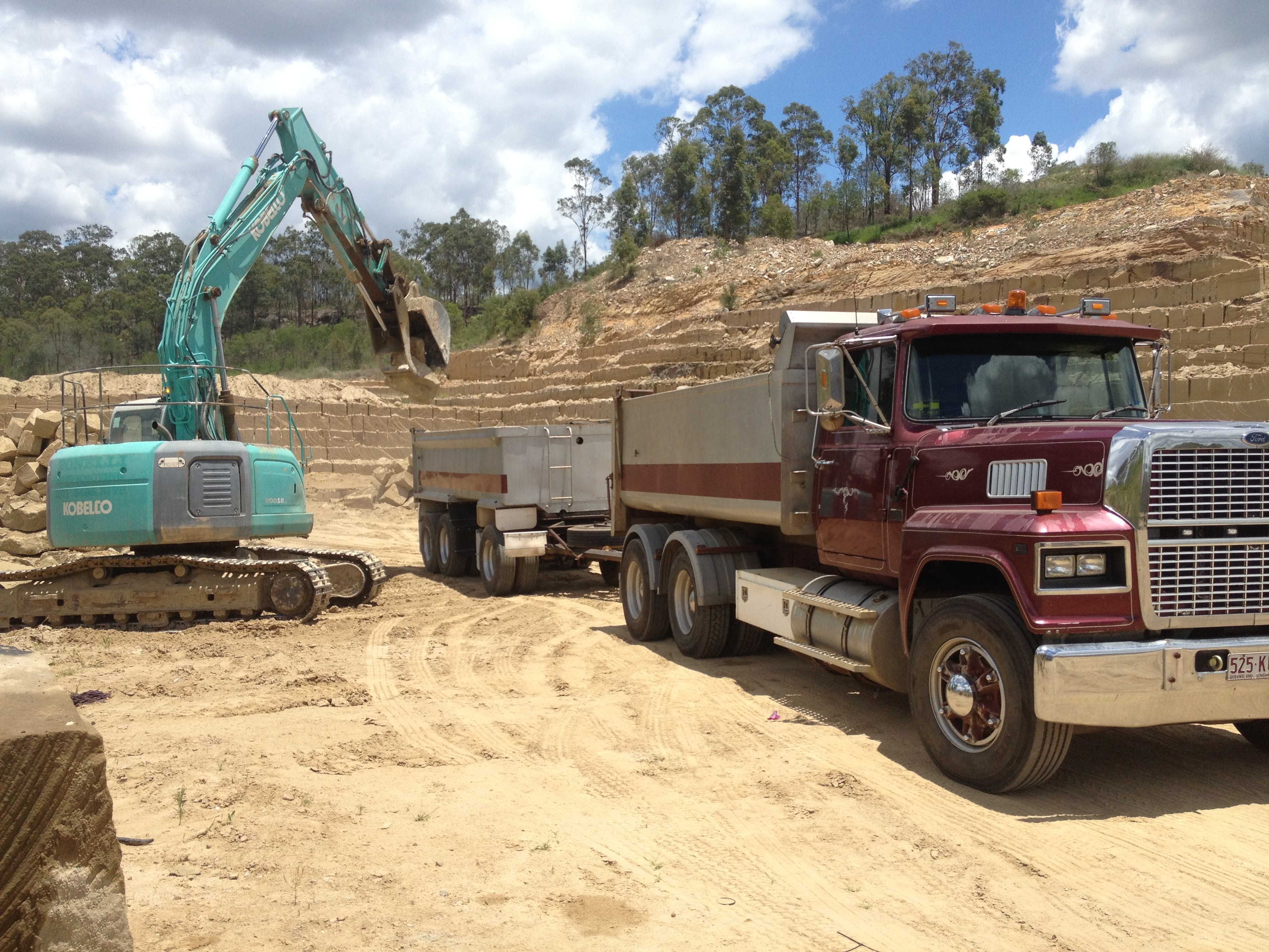 Kobelco excavator loading sandstone into dump truck on site
